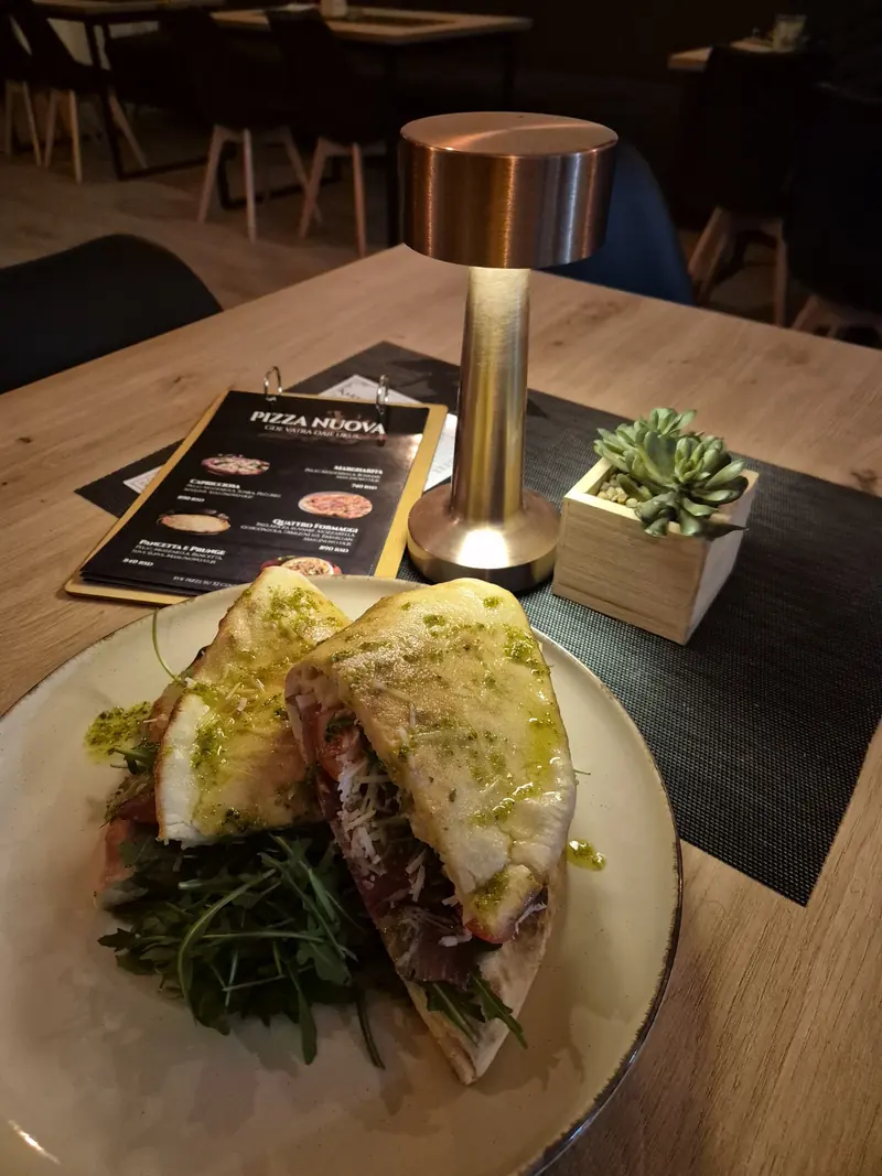 Sendvič sa pestom na stolu, pored bakarne lampe i jelovnika Pizza Nuova